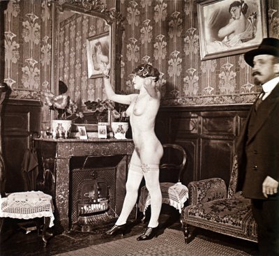 Photographie énigmatique montrant une jeune femme complètement nue (sauf ses chaussures et ses bas) recoiffant ses cheveux devant un miroir en présence d