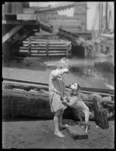 Garçon pieds nus, possiblement William Gray Hassler, jouant avec un chien sur le rivage d