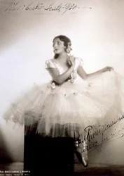 Portrait de la ballerine classique Rosa Piovella Ansaldo, en tutu et chaussons de ballet. Elle est assise, de face, le visage tourné sur le côté. Des roses en tissu décorent son vêtement et ses cheveux soigneusement coiffés (Milan, Teatro alla Scala)