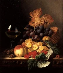 Un panier de raisins, framboises, une pêche et un verre de vin sur une table