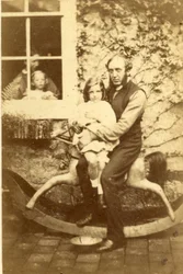 Père et fille assis sur un cheval à bascule avec frère et mère regardant par la fenêtre, années 1860