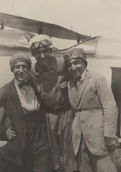 [Portrait de trois hommes souriant devant un avion].