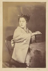 [Femme japonaise assise tenant un album de cartes-de-visite à une table].