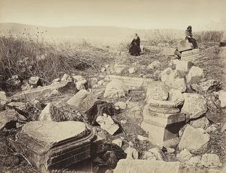 Un moine et un homme avec un fusil posent, assis sur des ruines, près de Capharnaüm