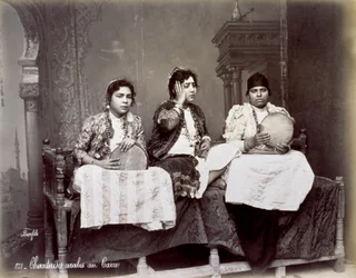 Portrait de trois jeunes chanteurs arabes en tenue ethnique avec de longs colliers. Ils posent dans le studio, assis. Deux d
