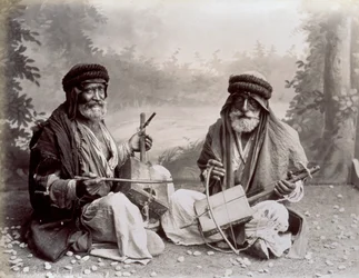 Portrait de deux musiciens arabes en tenue ethnique modeste. Les hommes âgés posent dans le studio, assis par terre. Derrière eux, un décor de paysage boisé