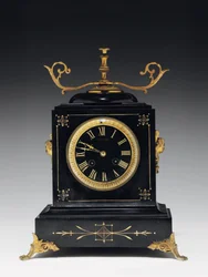 Pendule de cheminée en pierre noire, avec décoration incisée, avec pieds, ornements et accessoires en laiton doré, par Jausions de Pau, France, vers 1876-78