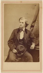 [Homme non identifié avec une barbiche, assis, tenant un chapeau sur ses genoux].
