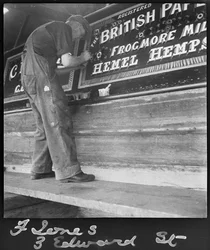 Frank Jones, en train de peindre le panneau des noms sur une péniche, 20e siècle (photo)