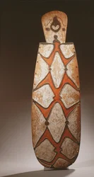 Bouclier ovale Asmat, sculpté en relief avec des figures stylisées, un masque en haut
