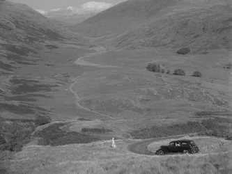 Une femme surplombe une vallée ouverte, avec une voiture garée à proximité.
