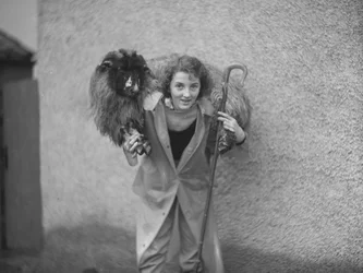 Une femme se tient debout avec un mouton en bandoulière et tient une houlette de berger.