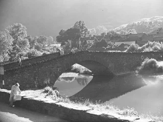 Femme assise sur un mur étudiant une carte avec une rivière et un pont en pierre en arrière-plan