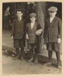[Trois garçons dans la rue de la ville en culottes et bonnets]