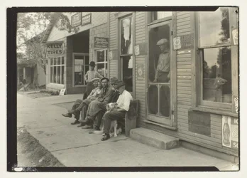 Hommes avec chien assis sur un banc devant un magasin général