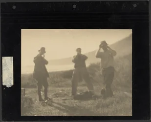 [Trois hommes debout sur une colline, les mains devant le visage]