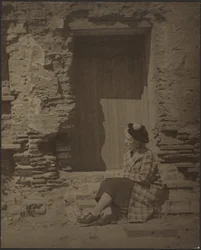 [Femme assise devant un bâtiment en ruine]