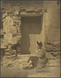 [Femme assise devant un bâtiment en ruine]