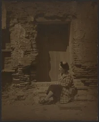 [Femme assise devant un bâtiment en ruine]