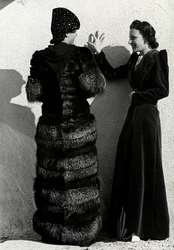 Deux mannequins présentent des créations de la maison de couture italienne "Dragoni". Un mannequin vu de dos porte un manteau en renard argenté. L