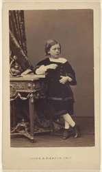 [Petite fille non identifiée debout, le coude posé sur un livre fermé posé sur une table].