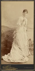 [Femme non identifiée portant une longue et élégante robe blanche, debout]