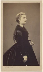 [Femme non identifiée portant une robe sombre, debout, de profil]