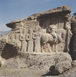 Relief rocheux représentant Shapur I (241-272 ap. J.-C.) et sa famille portant des emblèmes héraldiques sur leurs chapeaux, avec une inscription trilingue sur le cheval en grec, parthe et moyen-perse