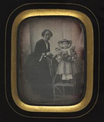 Enfant debout sur une chaise tenant des fleurs, avec sa mère, vers 1855