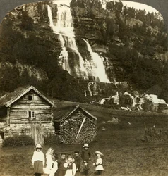 Enfants jouant dans un champ de fermier avec la cascade en terrasses de Tvinde, Vossevangen, Norvège, vers 1905