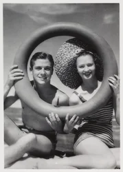 Homme et femme regardant à travers une bouée sur la plage, vers 1935