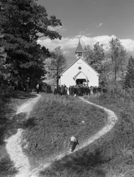 Hommes rassemblés devant un petit bâtiment rural, une école ou une église avec cloche