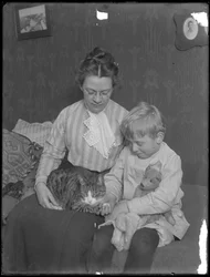 Harriet E. Hassler et William Gray Hassler, assis avec un chat tigré (Reddy) et un ours en peluche, c.1911