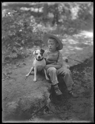 William Gray Hassler en chapeau de paille et salopette, posé assis dans les bois avec un petit chien (Bessie), 20 août 1911